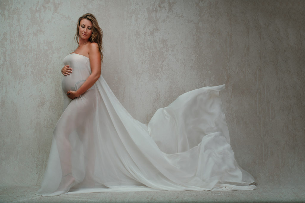 pregnant woman studio maternity with white fabric being tossed in the air light backdrop long hair