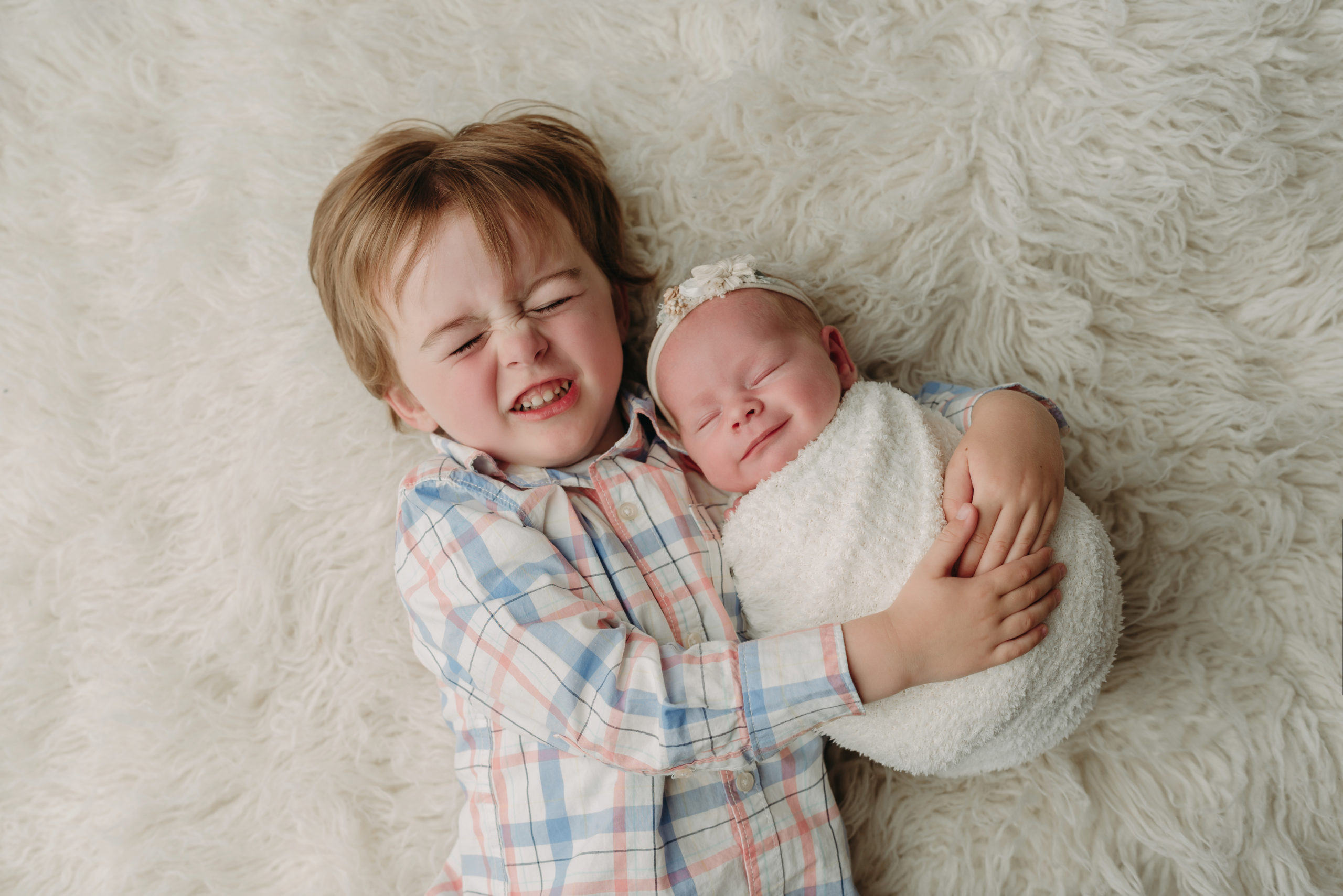 big brother sibling with newborn baby sister both smiling lying on flokati rug