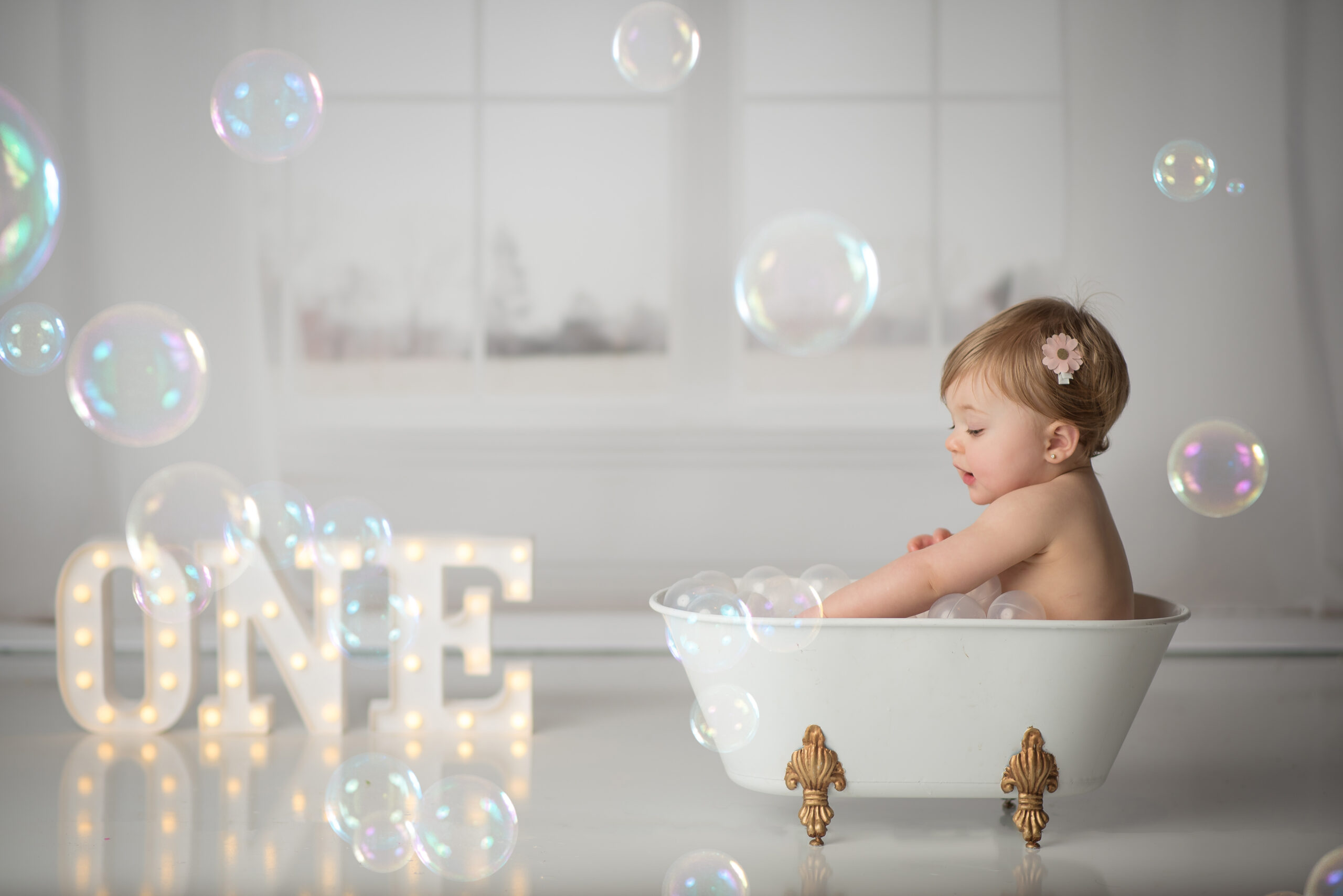 baby in bubble bath in ront of white windows with lit up one sign